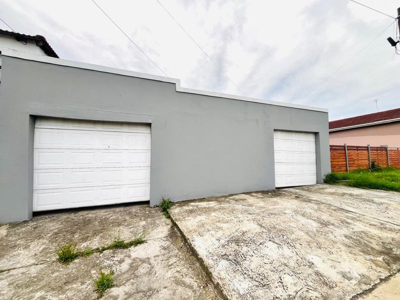 Exterior view of a double garage with white sectional doors and a weathered concrete driveway.