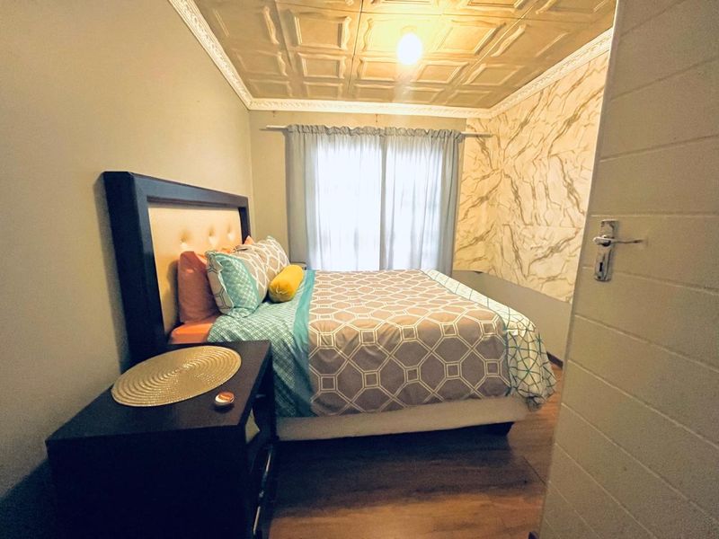 A cozy bedroom featuring a decorative coffered ceiling with crown molding, marble-effect wall paneling, and durable laminate flooring.