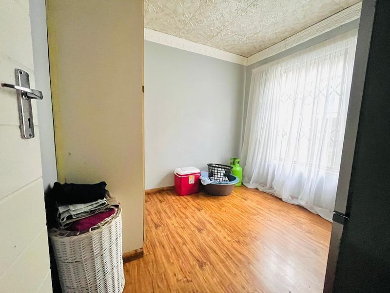 A vacant bedroom featuring laminate flooring, textured ceiling tiles, and a large window fitted with a security gate.