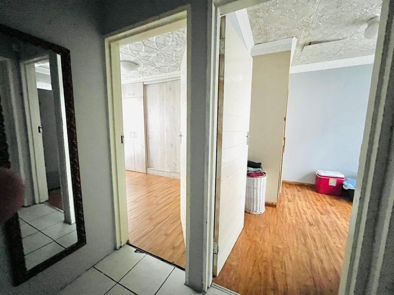 A hallway view showing access to two bedrooms with laminate flooring, built-in cupboards, and decorative textured ceilings.