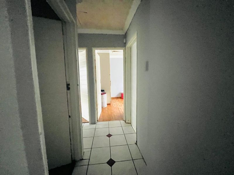 A narrow interior hallway featuring tiled flooring and multiple doorways leading to adjacent rooms, showing signs of wear and ceiling discoloration.