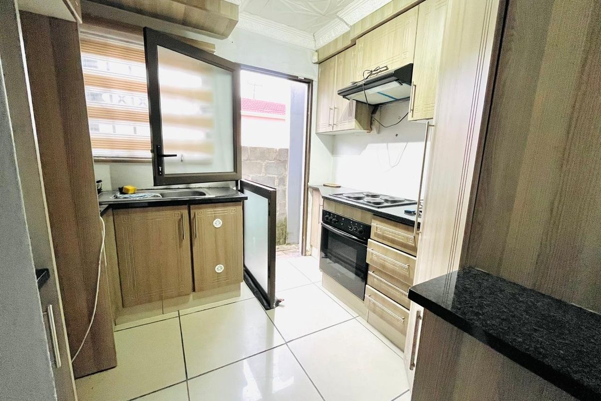Compact kitchen featuring wood-finish cabinetry, granite countertops, built-in oven and hob, and direct access to an outdoor area.