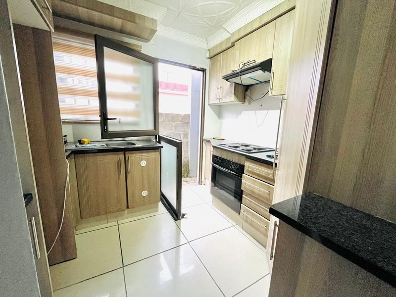 Compact kitchen featuring wood-finish cabinetry, granite countertops, built-in oven and hob, and direct access to an outdoor area.