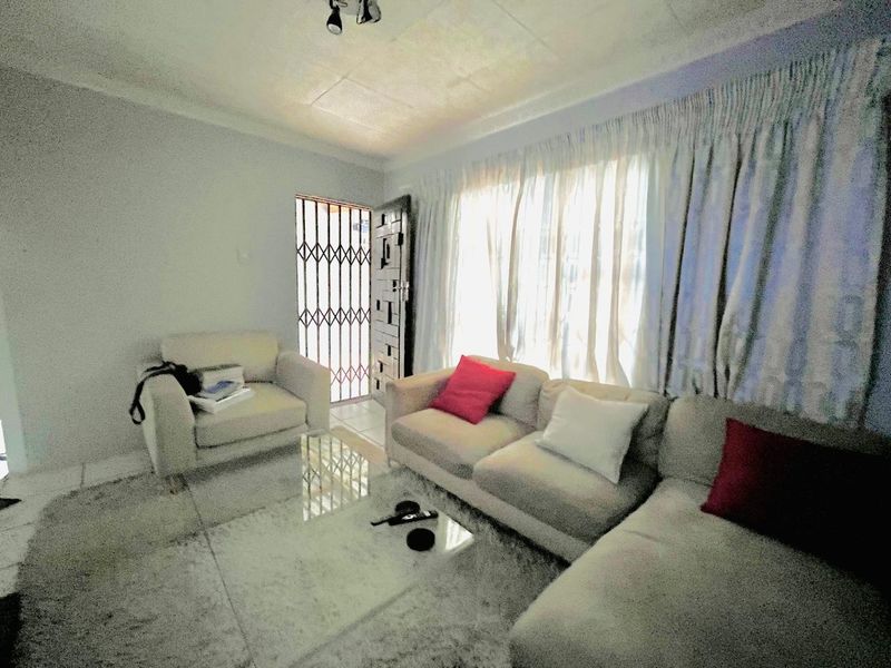 A living room featuring tiled flooring, a security gate at the entrance, and natural light through large windows.