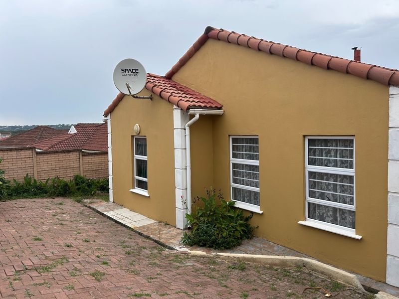 Front exterior view of a townhouse featuring a terracotta tiled roof, paved driveway, and security-fitted windows.