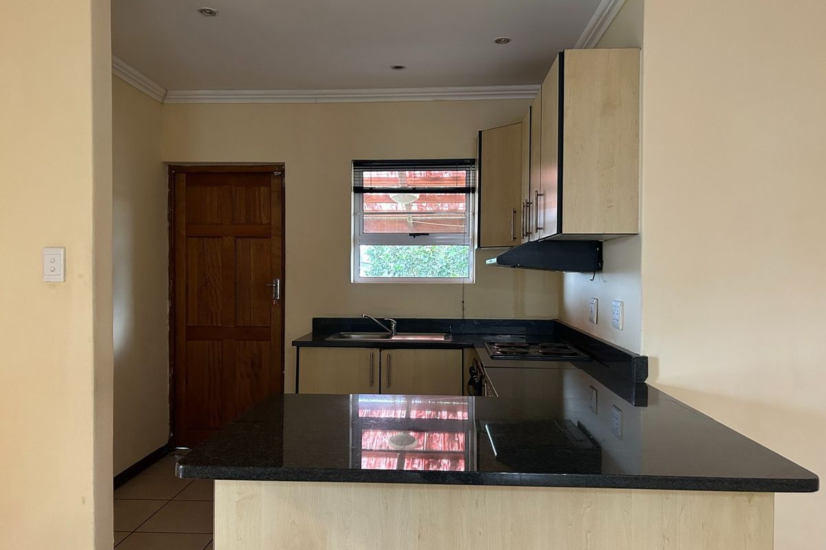 A functional kitchen featuring granite countertops, built-in cabinetry, an integrated hob, and an extractor fan, offering a clean and practical workspace.