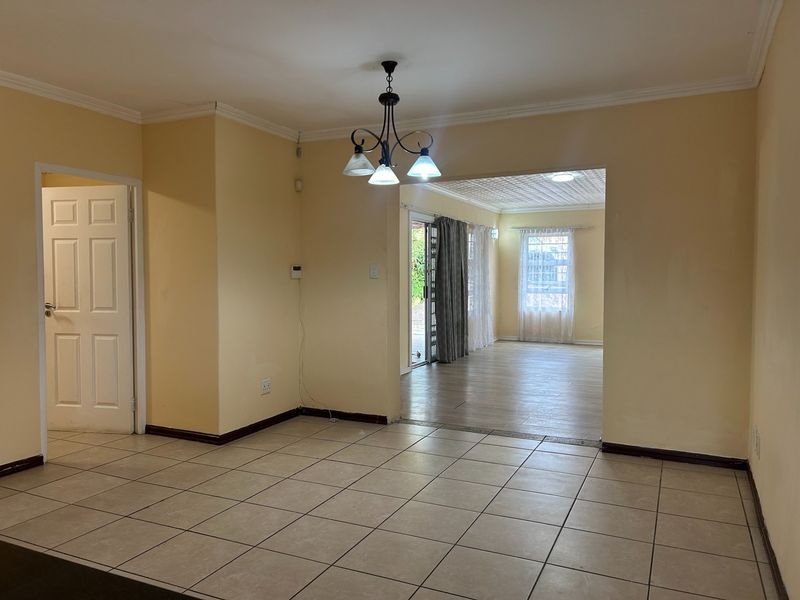 Spacious open-plan living area featuring tiled and laminate flooring, neutral wall tones, and direct access to the outdoor area through a sliding glass door.