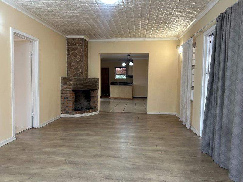 Spacious living area featuring a brick fireplace with stone detailing, laminate flooring, and a textured ceiling, leading through to an open-plan kitchen area.