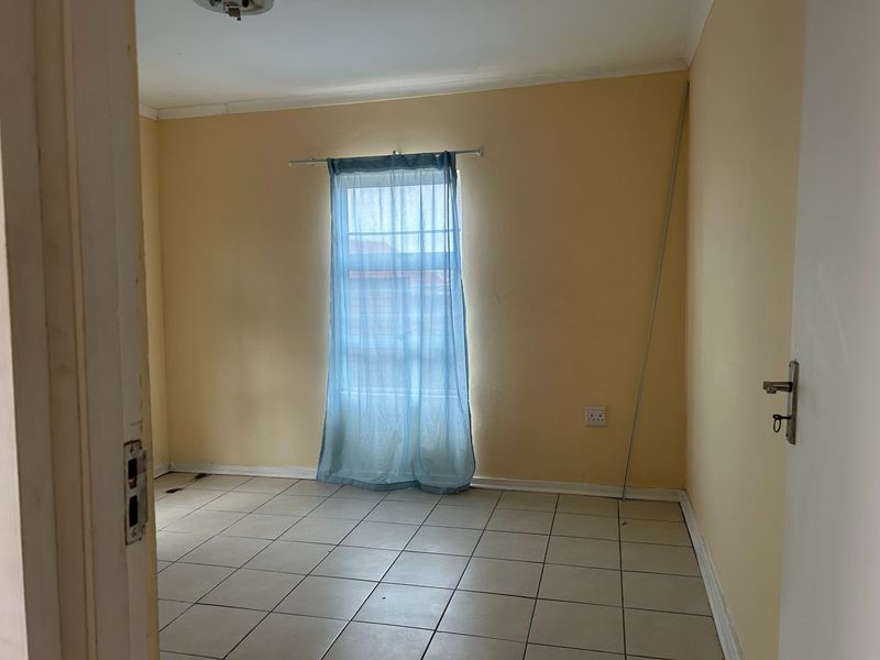 An empty bedroom featuring tiled flooring, neutral wall paint, and a single window, providing a blank canvas for potential interior design updates.