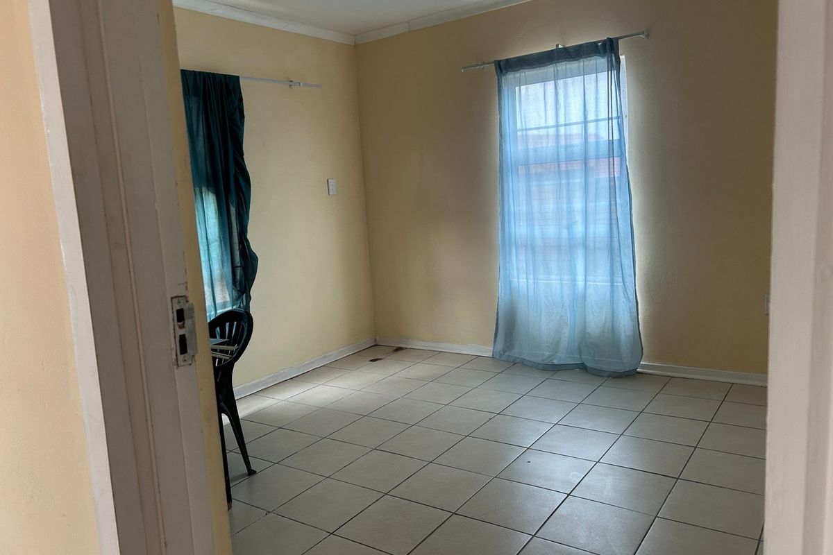 An empty bedroom featuring neutral tiled flooring and dual windows with existing curtain rods, offering a blank canvas for personalization.
