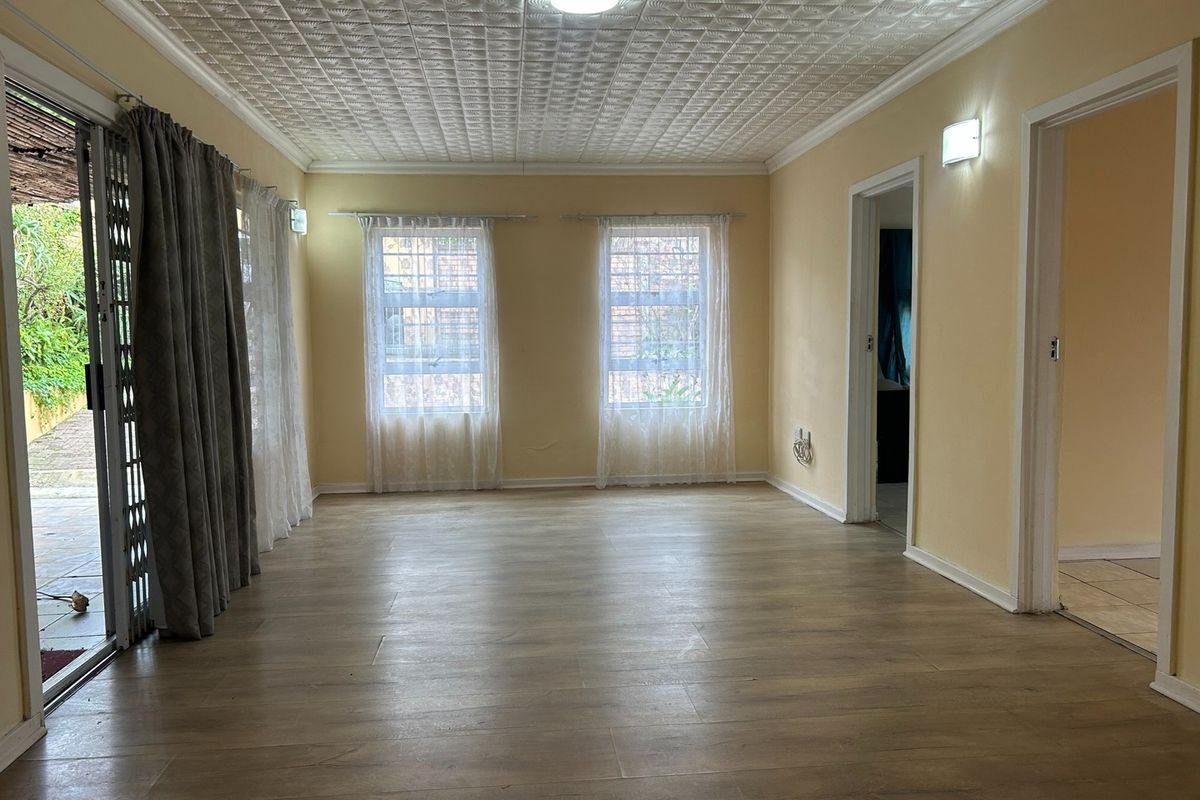 An empty living room featuring laminate flooring, textured ceiling tiles, and large windows providing natural light with access to an outdoor patio area.