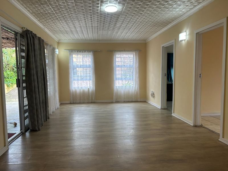 An empty living room featuring laminate flooring, textured ceiling tiles, and large windows providing natural light with access to an outdoor patio area.