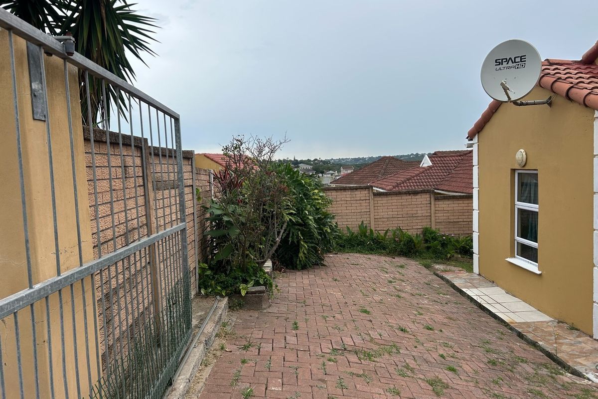 A rear exterior view of the townhouse featuring brick paving, a boundary wall, and a satellite dish mounted on the exterior wall.