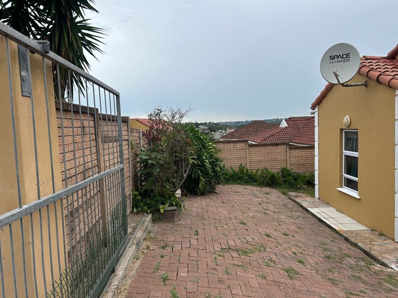 A rear exterior view of the townhouse featuring brick paving, a boundary wall, and a satellite dish mounted on the exterior wall.