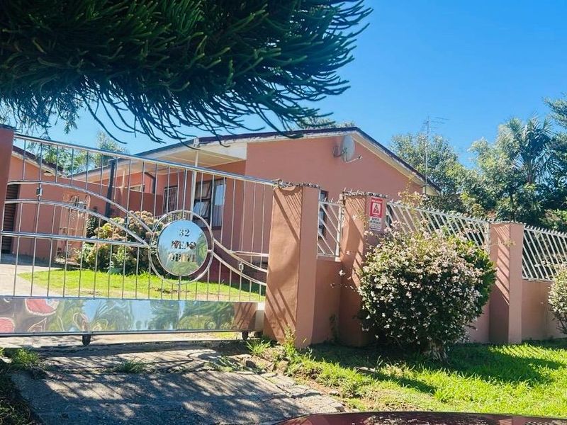Front view of the property featuring a secure metal gate, perimeter wall with security spikes, and a paved driveway leading to the house.