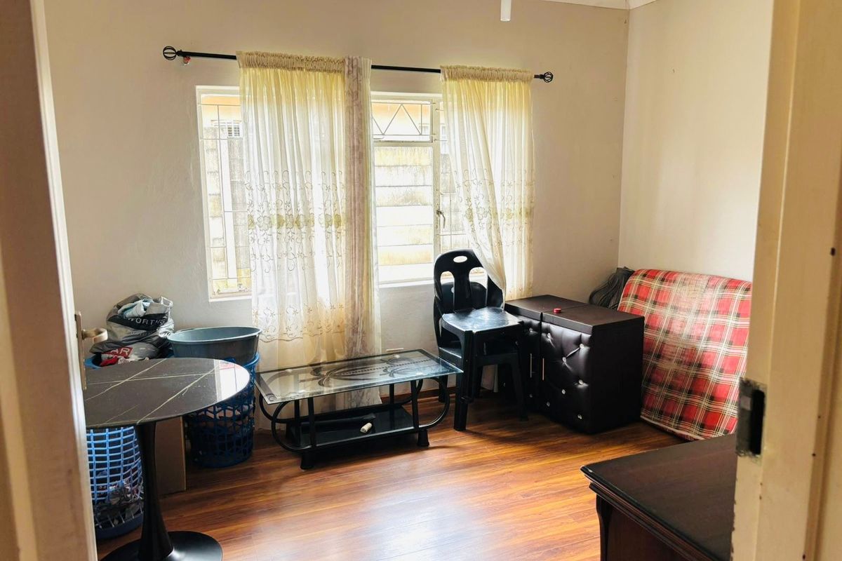 A living room featuring laminate flooring and steel-framed windows with security bars, offering a functional space ready for modernization.
