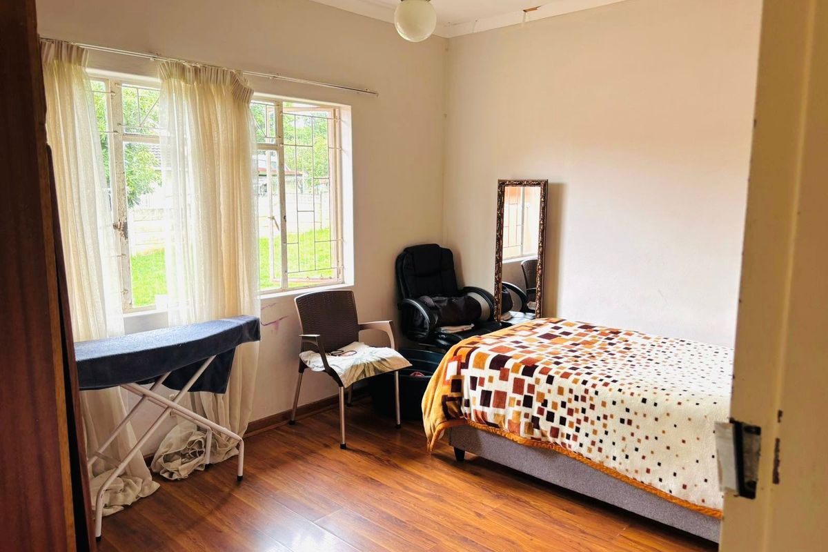 A functional bedroom featuring laminate flooring, natural light through large windows with security bars, and a standard ceiling light fixture.