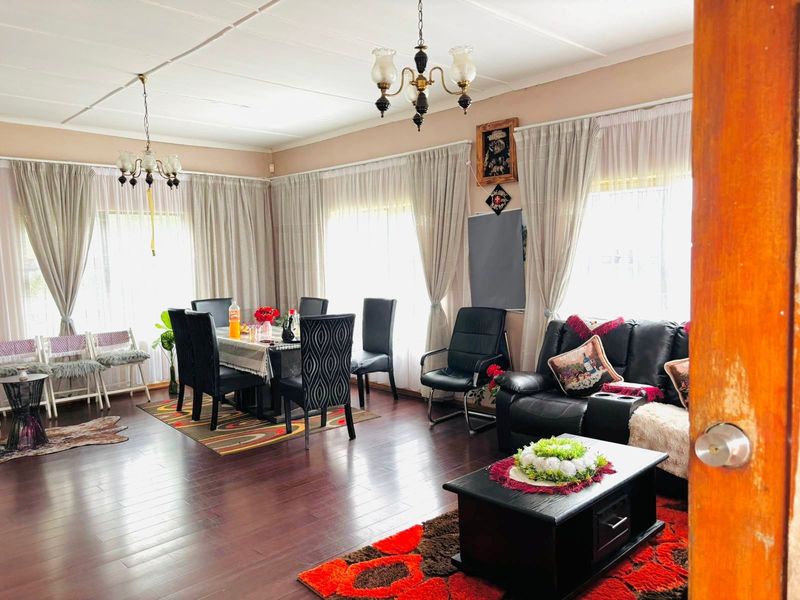 Spacious open-plan living and dining area featuring dark laminate flooring and multiple windows with curtain treatments, offering a versatile layout for family living.
