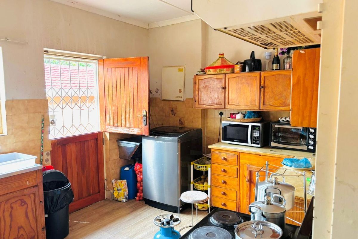 A functional kitchen featuring wooden cabinetry, tiled splashbacks, and direct access to the exterior via a timber door with a security gate.