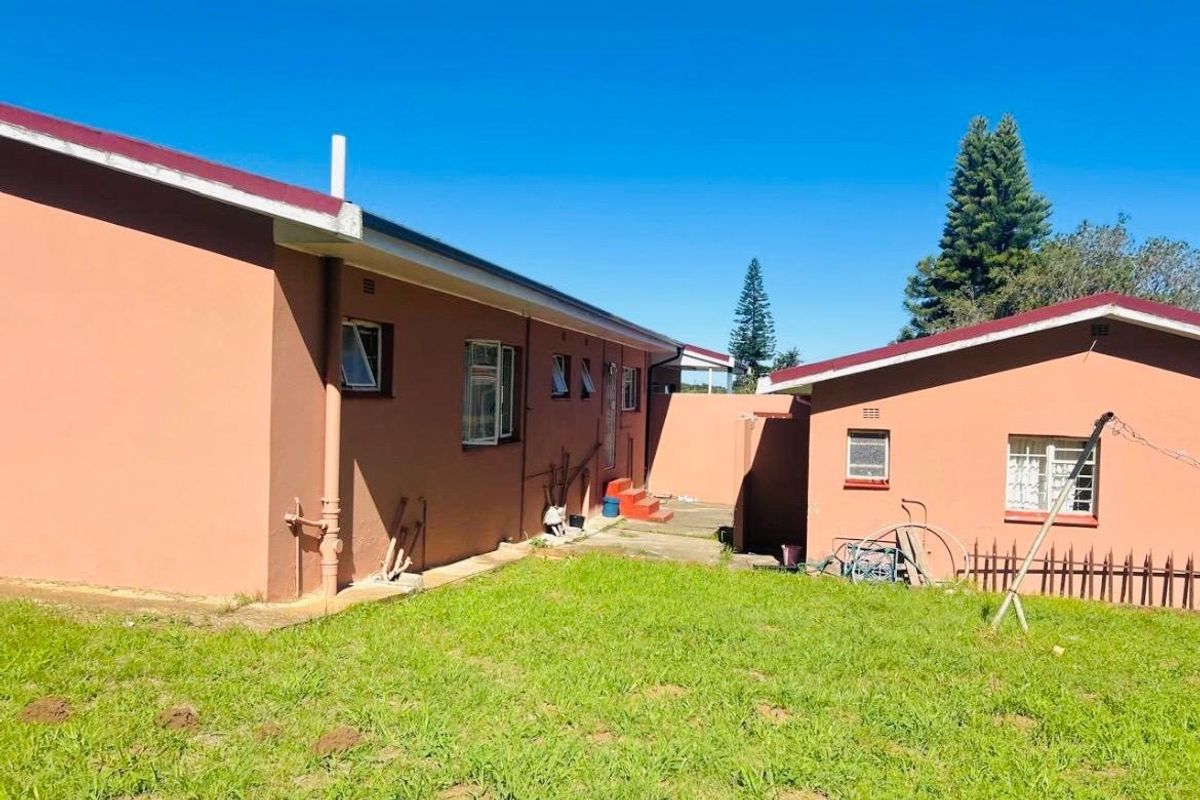 Rear view of the property showing the exterior walls, metal window frames, and a concrete pathway leading to the backyard area.