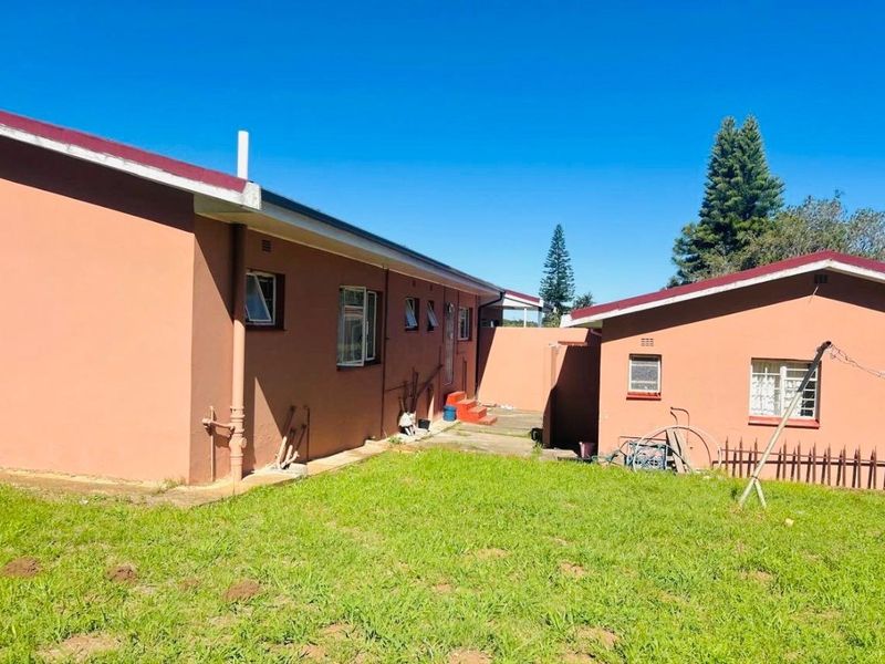 Rear view of the property showing the exterior walls, metal window frames, and a concrete pathway leading to the backyard area.