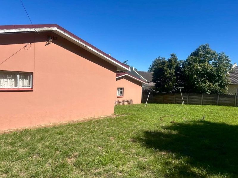 Rear view of the property showing the exterior wall, lawn, and boundary wall fencing.