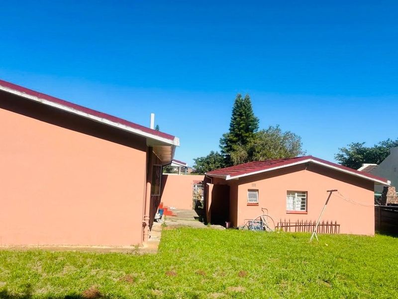 Rear view of the property showing the main house and a detached outbuilding with tiled roofs and a grassed backyard area.