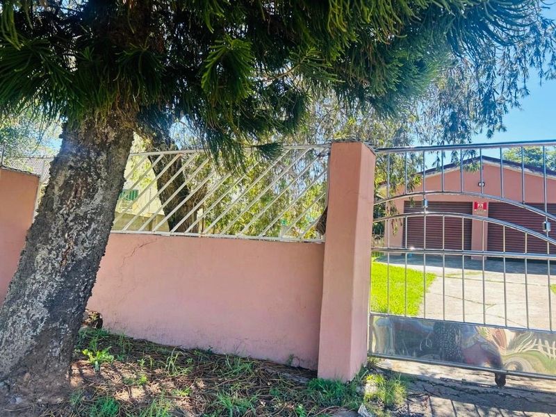 Front view of the property featuring a boundary wall with metal fencing, a stainless steel security gate, and a paved driveway leading to a garage.