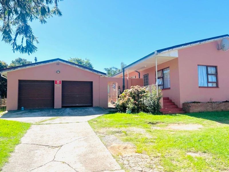 Front view of a single-story house featuring a double garage, concrete driveway, and a pink exterior finish with a small front garden.