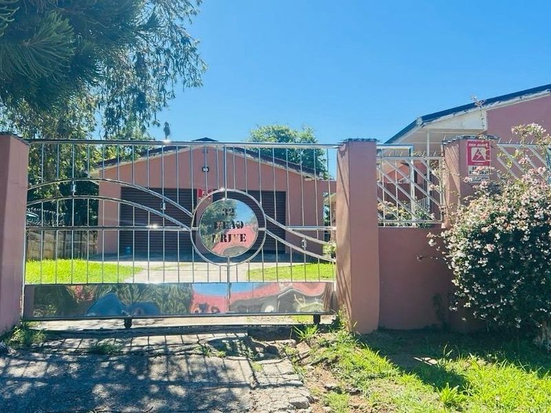Front view of the property featuring a stainless steel sliding gate, concrete driveway, and brick boundary wall.