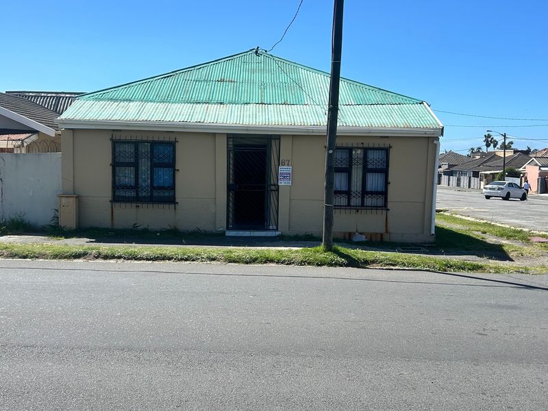 Front elevation of a single-story house featuring a corrugated metal roof, security bars on windows, and a security gate at the entrance.