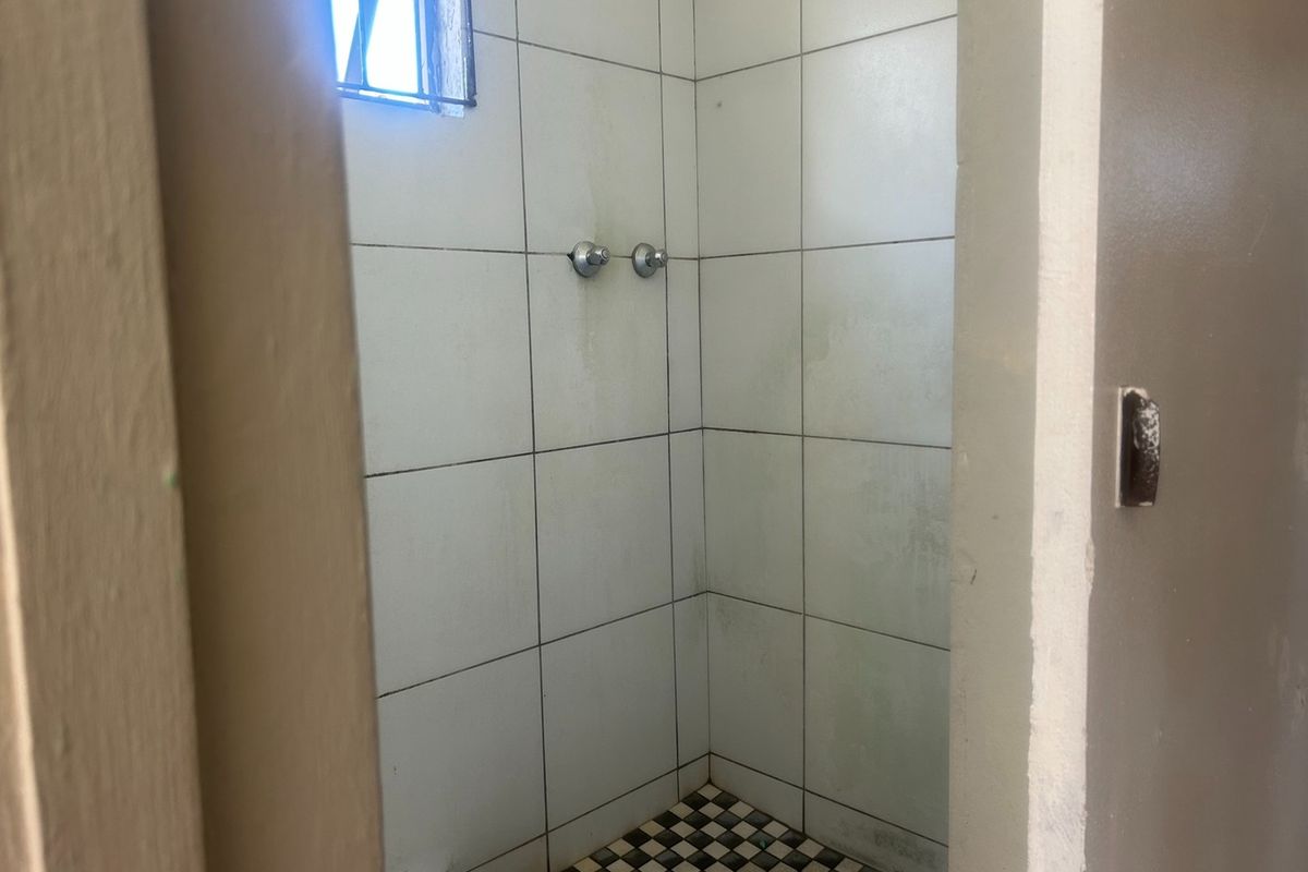 A compact shower enclosure featuring tiled walls and flooring, requiring cosmetic updates to improve its overall condition and appeal.