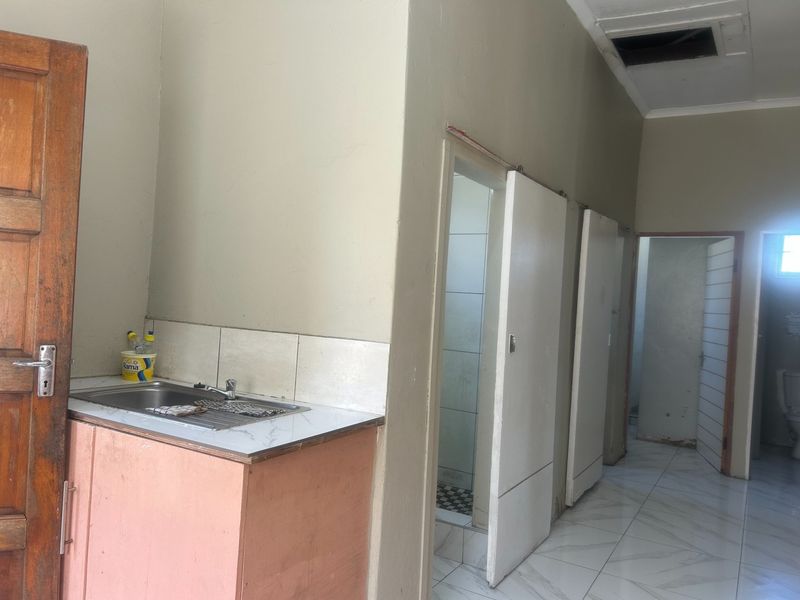 A functional kitchen area featuring a stainless steel sink, tiled flooring, and built-in cabinetry, requiring some cosmetic updates and ceiling repairs.