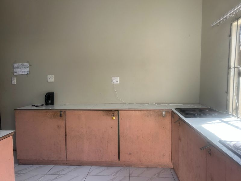 A functional kitchen space featuring built-in cabinetry, a countertop with an integrated hob, and tiled flooring, ready for cosmetic updates.