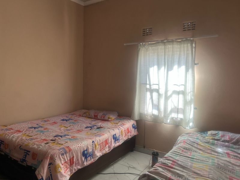 A bedroom featuring tiled flooring and natural light from a window with ventilation vents above.