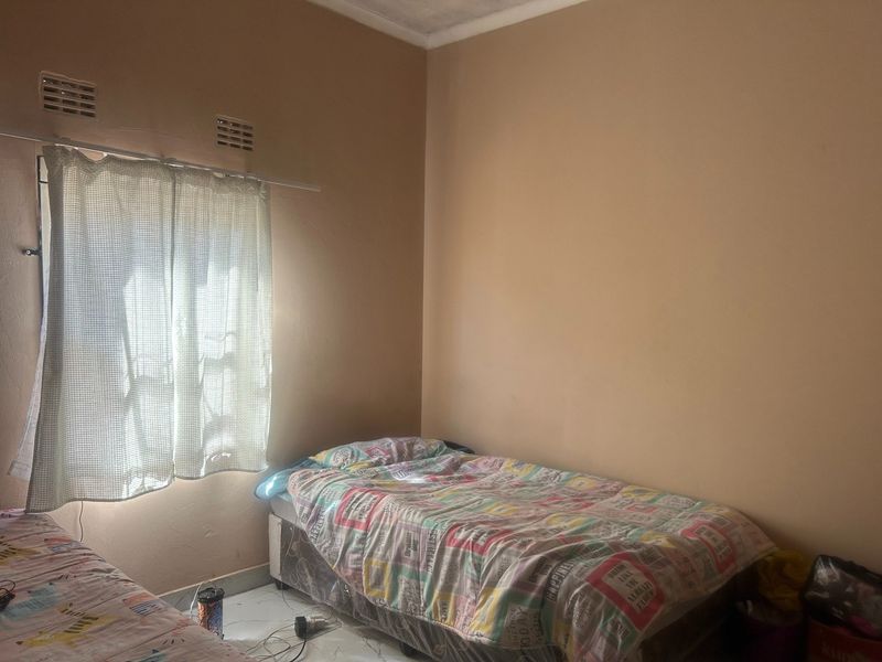 A simple bedroom featuring plain walls and a window with a curtain, providing a functional space for rest.