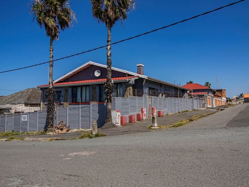 Street view of a guest house property featuring a perimeter wall with razor wire, a metal roof, and a paved driveway.