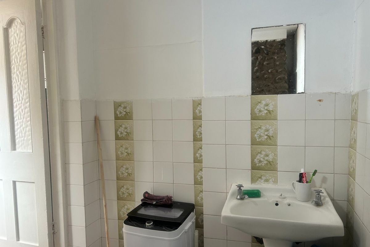 A functional bathroom featuring a pedestal washbasin and decorative ceramic wall tiling, requiring cosmetic updates to improve the overall finish.