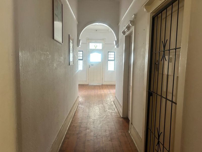 A long hallway featuring original timber flooring, an architectural archway, and a secure entrance door with a transom window.
