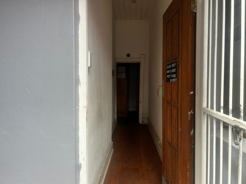 A narrow interior hallway featuring timber flooring and a solid wood door with a security gate.