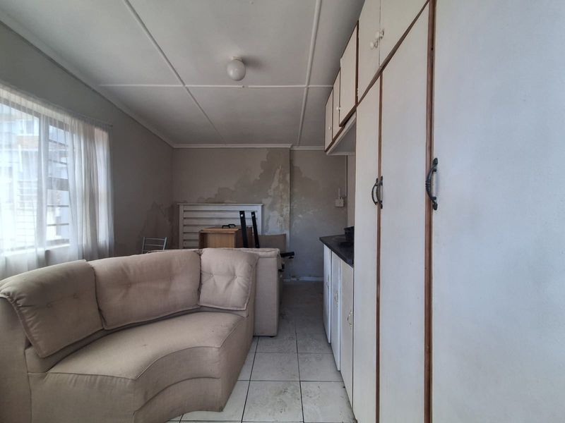 Open plan living area featuring built-in cabinetry and tiled flooring, currently showing significant wall surface damage and signs of wear.