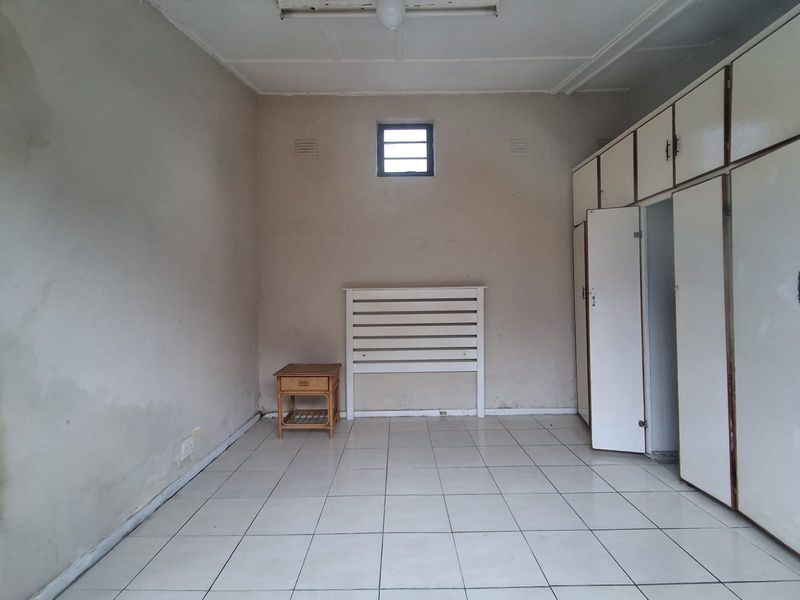 A sparsely furnished bedroom featuring tiled flooring, built-in storage cupboards, and a small high-level window, offering a blank canvas for renovation.