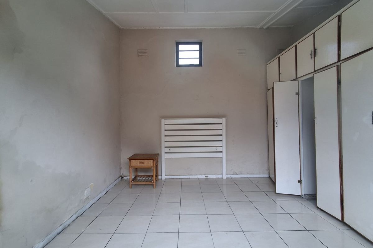 A sparsely furnished bedroom featuring tiled flooring, built-in storage cupboards, and a small high-level window, offering a blank canvas for renovation.