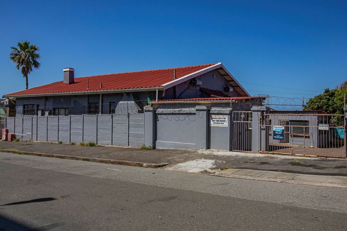Street view of the guest house property featuring a perimeter wall with security fencing, a metal gate, and a red corrugated metal roof.