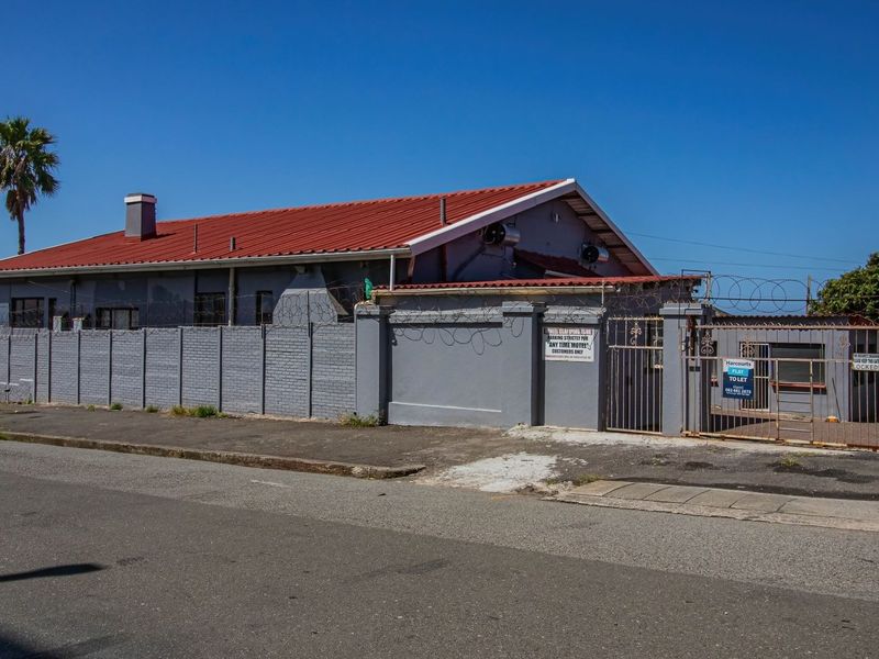 Street view of the guest house property featuring a perimeter wall with security fencing, a metal gate, and a red corrugated metal roof.