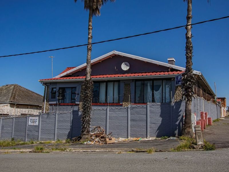 Front exterior view of a guest house property featuring a perimeter wall with razor wire and a metal roof structure.