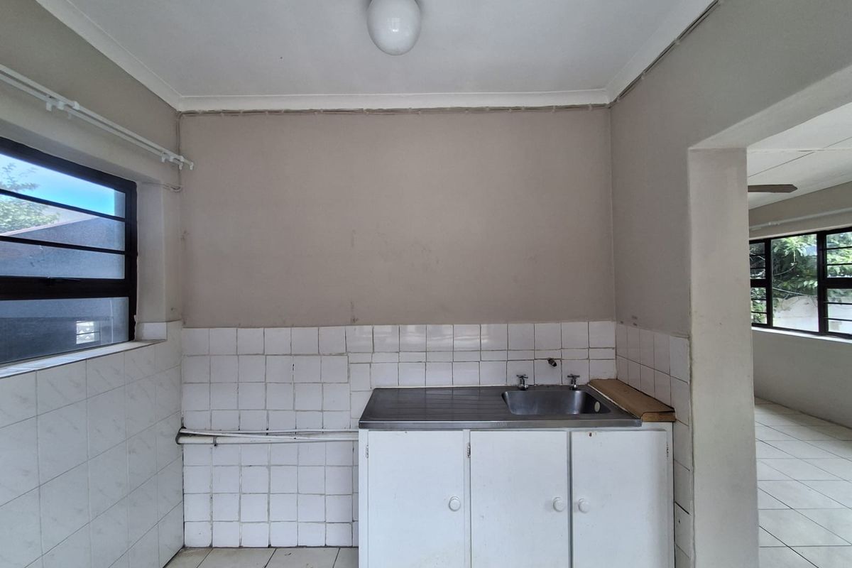 A compact, empty kitchen area featuring a stainless steel sink, tiled splashback, and basic built-in cabinetry, ready for renovation or modernization.