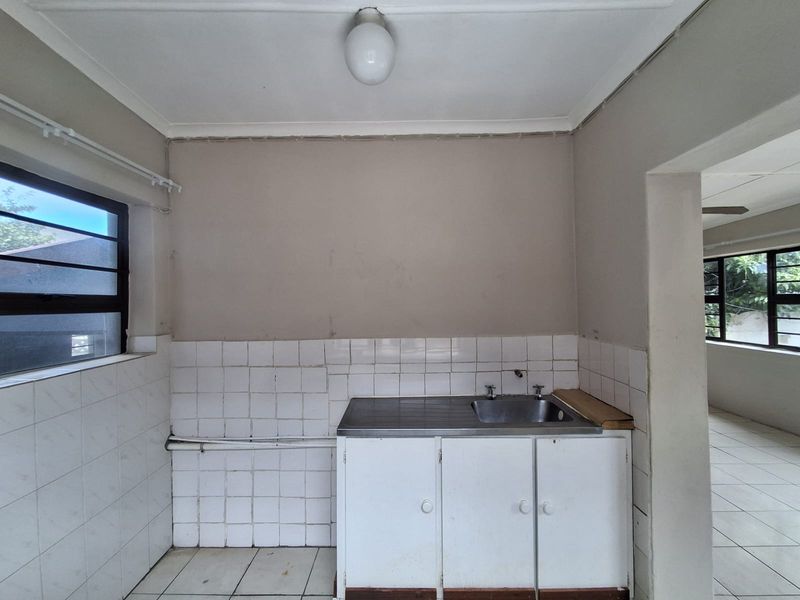 A compact, empty kitchen area featuring a stainless steel sink, tiled splashback, and basic built-in cabinetry, ready for renovation or modernization.