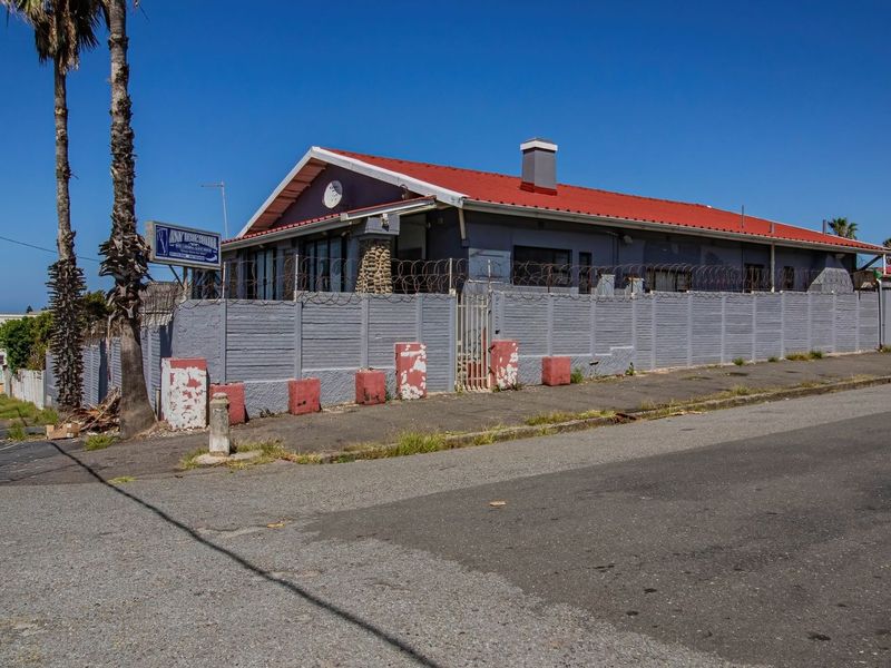 Street-level view of the guest house exterior featuring a metal roof, perimeter wall with security fencing, and prominent signage.