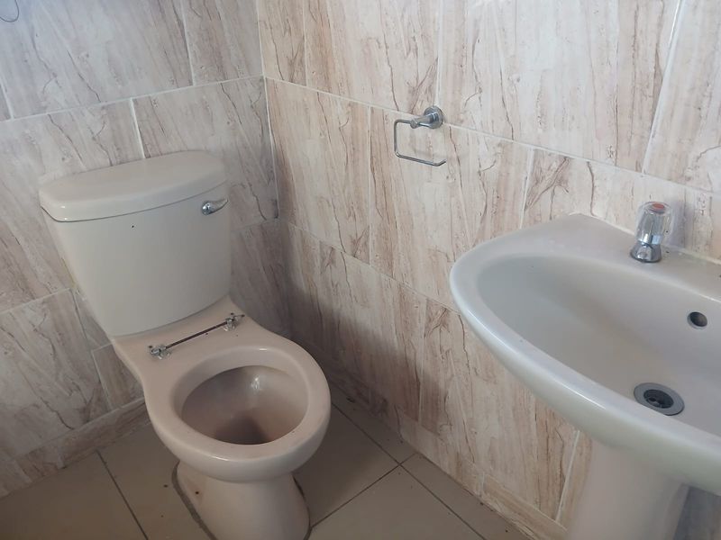A compact bathroom featuring a pedestal basin and toilet with full-height ceramic wall tiling.